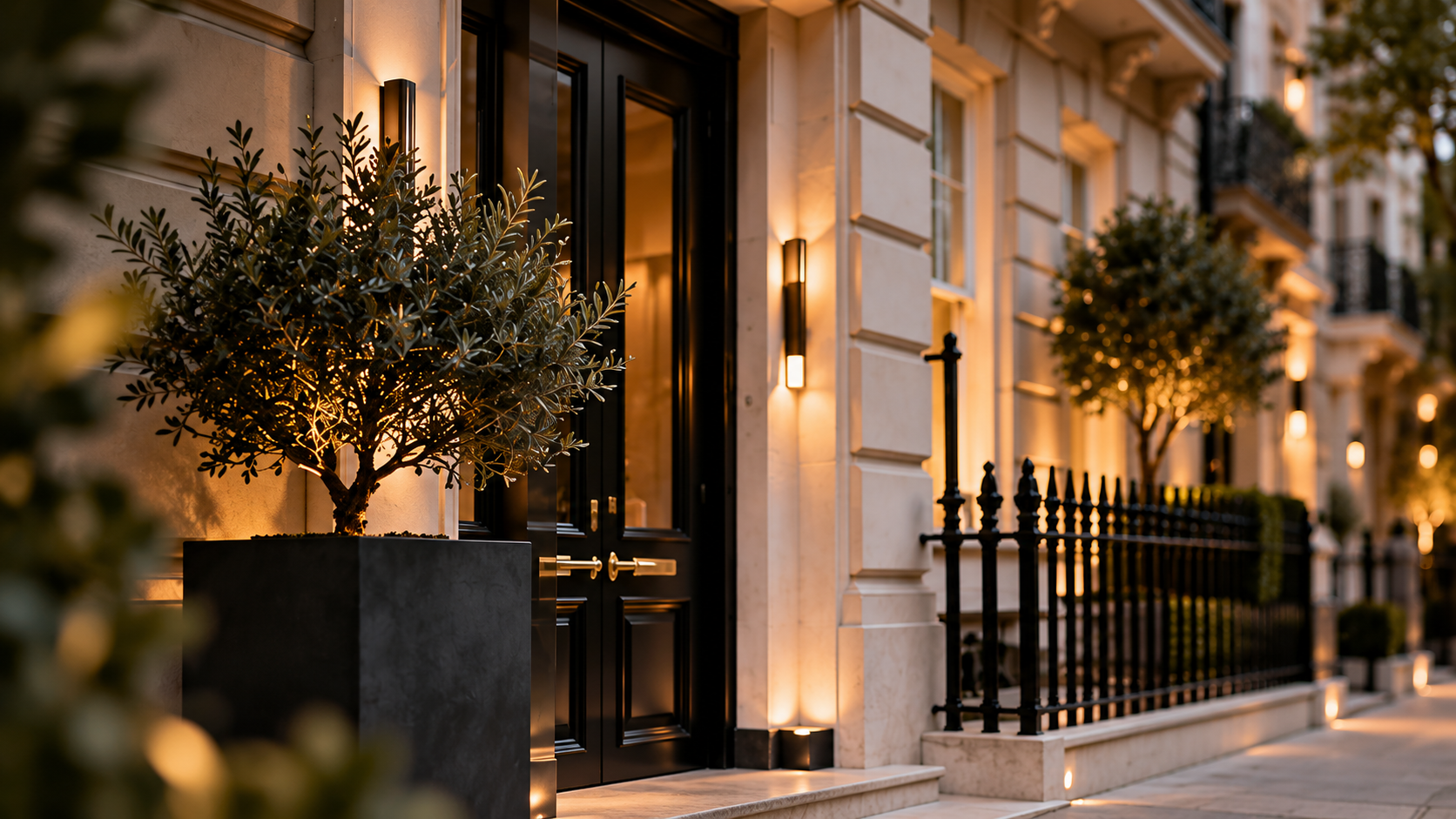 Stucco townhouse entrance with olive tree and black railings at dusk